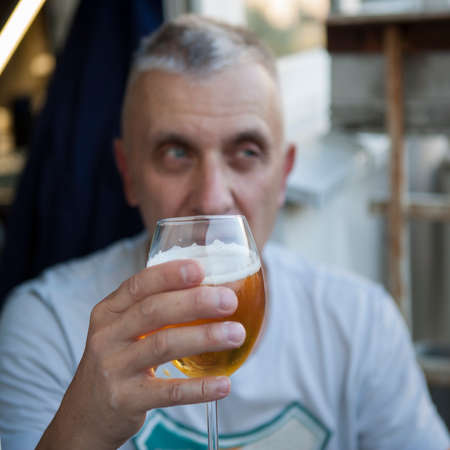 A man posing with a lager in his hand, focus in the foreground