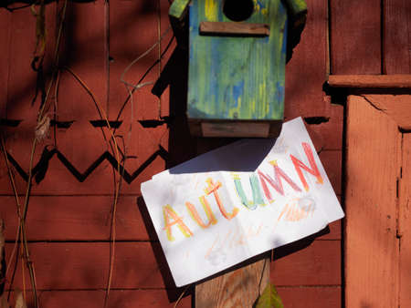 A word Autumn written on a paper and empty birdhouse on the wall, concept of season shiftの写真素材