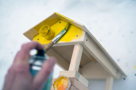 selective focus shot of a hand with spray paint and a wooden birds feeder