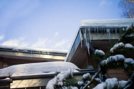 A rooftop and hanging icicles against the springtime sky