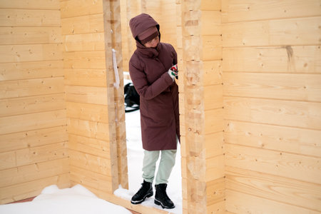 A young female in winter clothes standing in a doorway of unfinished wooden houseの写真素材