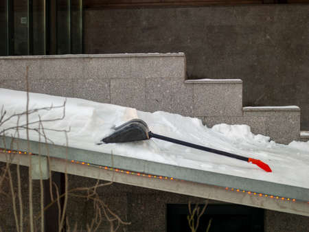 Removing snow from a ledge outside a house, abandoned shovel out of focus in the center of compositionの写真素材