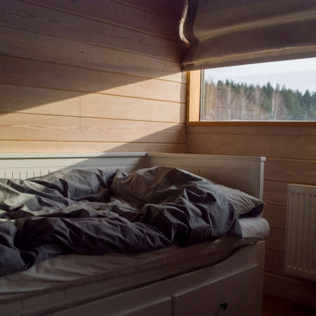 Unmade bed close to window full of morning light, indoor shotの写真素材