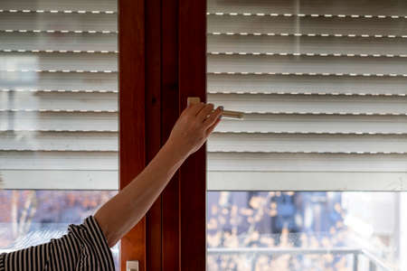 Female hand about to open a window with blind, indoor cropped imageの写真素材