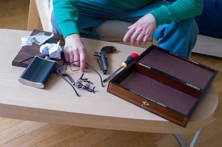 A man servicing old handguns on a desk with scattered tools, concept of hobby