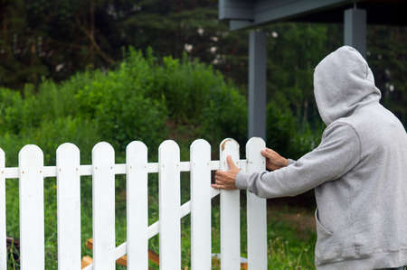 A man in hood closing or opening white timber gate, outdoor shotの写真素材