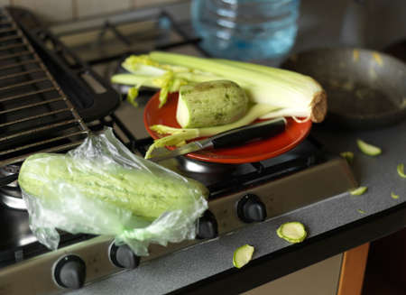 Stove top and zucchini about to be chopped in a messy kitchen, shallow dof