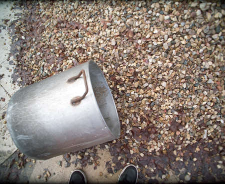 Human feet standing next to a gravel pile and casserole for it handling