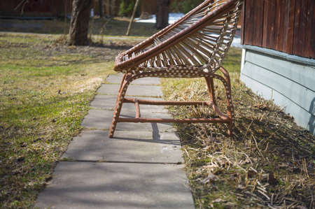 Warm sunny day shot of a wicker chair placed on a footpath in a gardenの写真素材