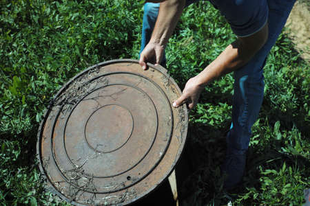A worker removing a top of a sewage inspection hole, summertime outdoor shot