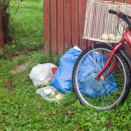 A bicycle and plstic bags full of household rubbish leanaed against the wooden fence