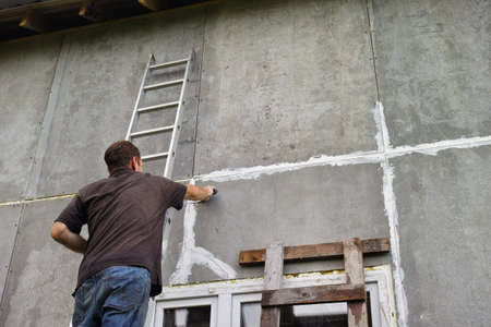 a worker standing on ladder and sealing seams in house wallの写真素材