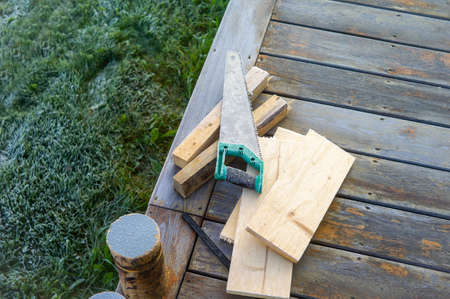 firewood and handsaw covered with ice and abandoned on a hardwood floor of verandaの写真素材