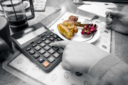Closeup of a woman calculating by one hand and eating with another, selective color image