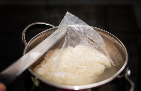 taking a sachet with rice out of a boiling water with a kitchen knife, macro shotの写真素材