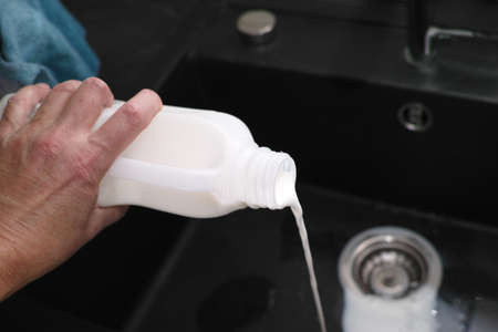 a hand pouring milk into a kitchen sink, indoor macro shotの写真素材