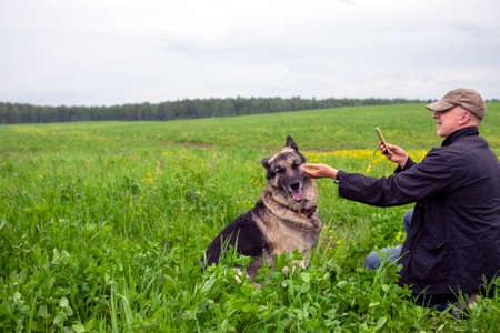 a man taking photo of his dog on mobile phone, outdoor shotの写真素材