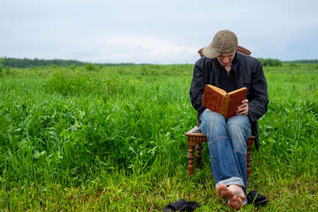a man with bare feet reading a book while sitting outdoorsの写真素材