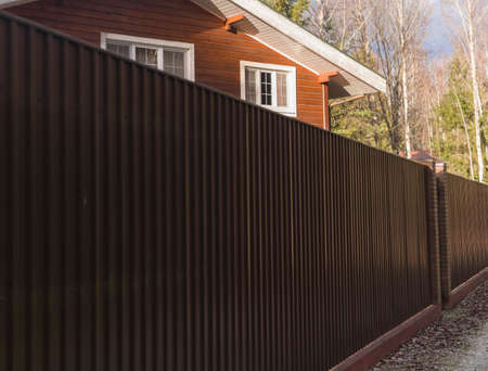 a solid metal fence and a part of house behind it, concept of neighborhoodの写真素材