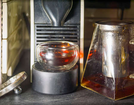 A coffeemaker, glass with coffee and a tea pot on a tableの写真素材