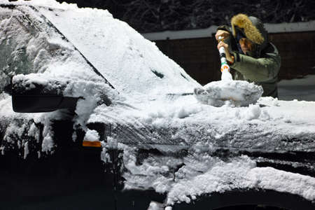 a man removing ice and snow from a windshield with brush, night sceneの写真素材
