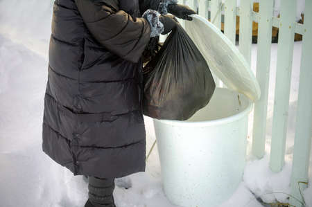 woman throwing plastic bag with garbage into a bin, winter sceneの写真素材