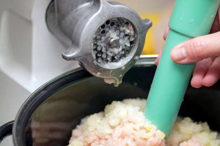 closeup of a mincer and a hand with plunger mixing minced meat with onionの写真素材