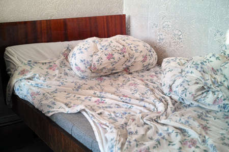 messy bedroom with unmade bed and crumpled beddingの写真素材