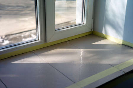 a windowsill with new tiles and protective adhesive tape, sunny day indoor close upの写真素材