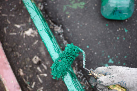 freshly pianted greeen fence and a roller for painting in a hand wearing gloveの写真素材