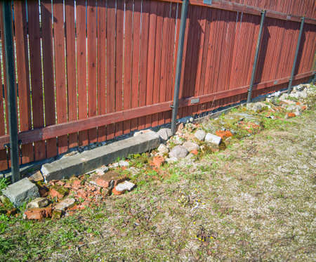 a wooden fence slightly leaning and strengthened with stones, outdoor sunny day shotの写真素材