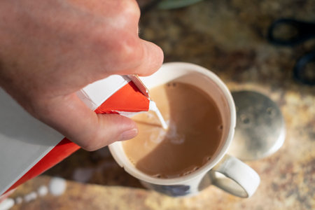 closeup shot of a hand holding pack of milk and pouring it into a coffee cupの写真素材