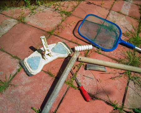 A swimming pool cleaning brush with broken handle and net placed on the groundの写真素材