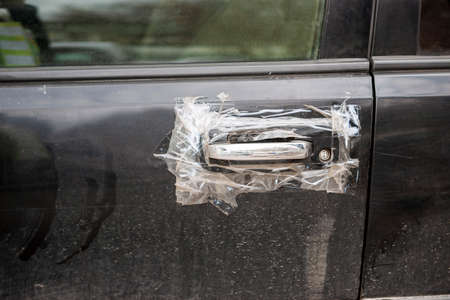 a damaged car door handle wrapped with adhesive tape, outdoor closeupの写真素材