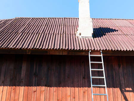 a steel ladder leaned against the roof and a chimney needs repairの写真素材