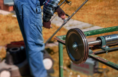 a handyman repairing old broken lawnmower outdoors, daylight shot with selective focusの写真素材