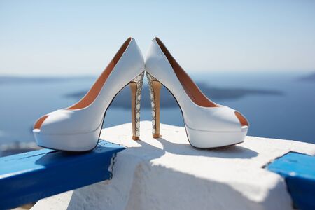the brideâs shoes are on the railing overlooking the sea and clear blue skyの写真素材