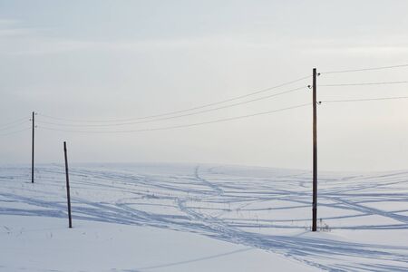Snow field crossed by tracks from passing cars and polesの写真素材