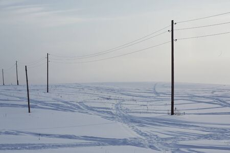 Snow field crossed by tracks from passing cars and poles.の写真素材
