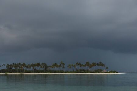 Stormy sky, turquoise water and a strip of white sandy beach with palm treesの写真素材