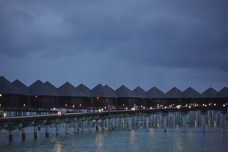 A row of bungalows with burning lanterns stand on stilts in the water.の写真素材