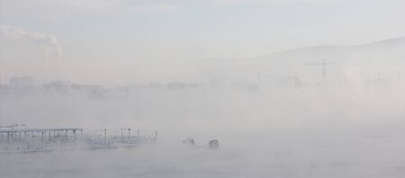 Fog over the winter river with various buildingsの写真素材