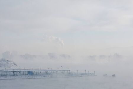 Winter landscape with foggy rivers is in the background of islands with trees, buildings and hills.の写真素材