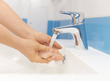 The girl washes her hands under running water in the bathroomの写真素材