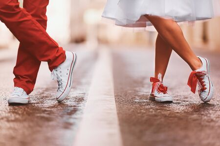 Newlyweds in sneakers are standing on the street. They crossed their legs.