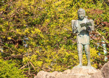 the statue of Ninomiya Sontoku (born - Ninomiya Kinjiro), showing him as a boy reading a book while walking and carrying firewood on his back, representing good virtues, hardworking and perseverenceの写真素材
