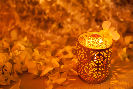 Candle lit in the beautiful container surrounded by blooming orchid flowers background. Decoration and accessories in wedding ceremony concept.の写真素材