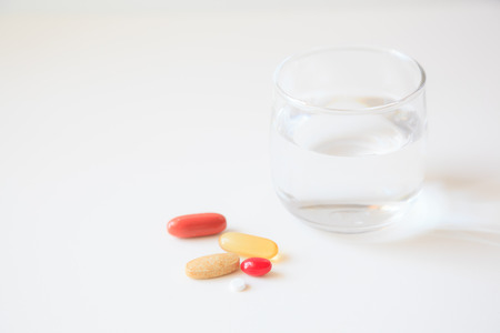 selective focus on a glass of water and medicine pills on white table background