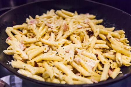 Delicious Creamy White Sauce Hearty Bacon Garlic Penne Pasta in frying skillet pan. Italian Pasta Dish, Gastronomy, Delicacy, Cuisine, Food, Meal, Dinner and Recipe conceptの写真素材