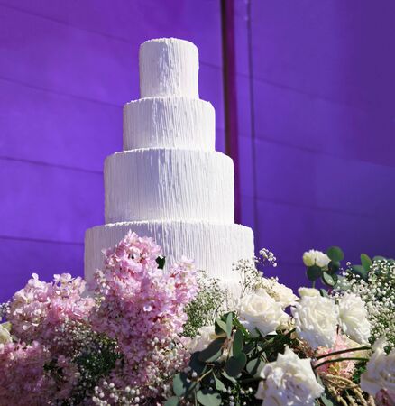Wedding Cake with beautiful flowers decoration at the stage in front of purple light backdrop in wedding reception night ceremony. Food Catering and Venue for Bridal Wedding and Marriage conceptの写真素材